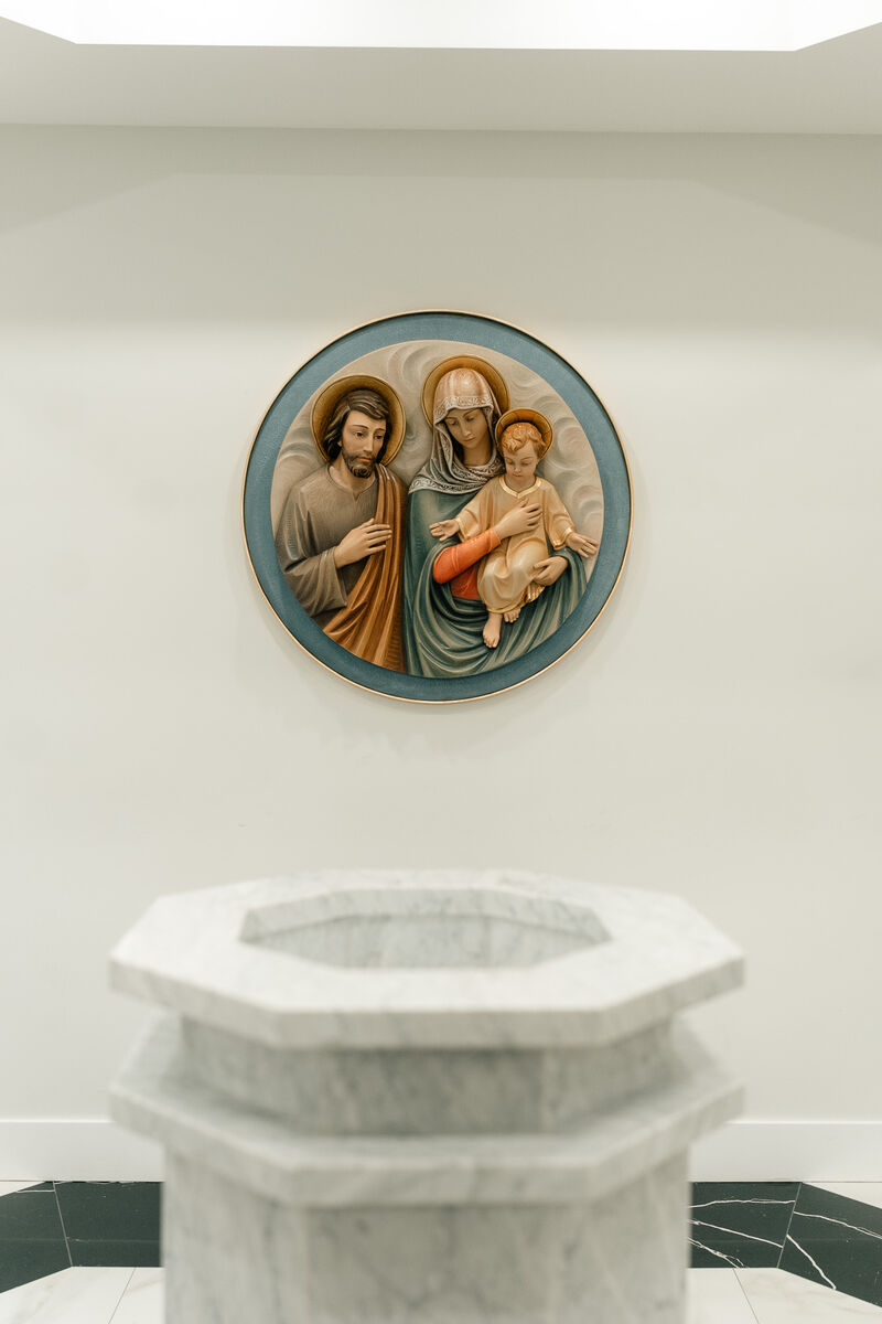 Marble baptismal font beneath the Holy Family relief medallion