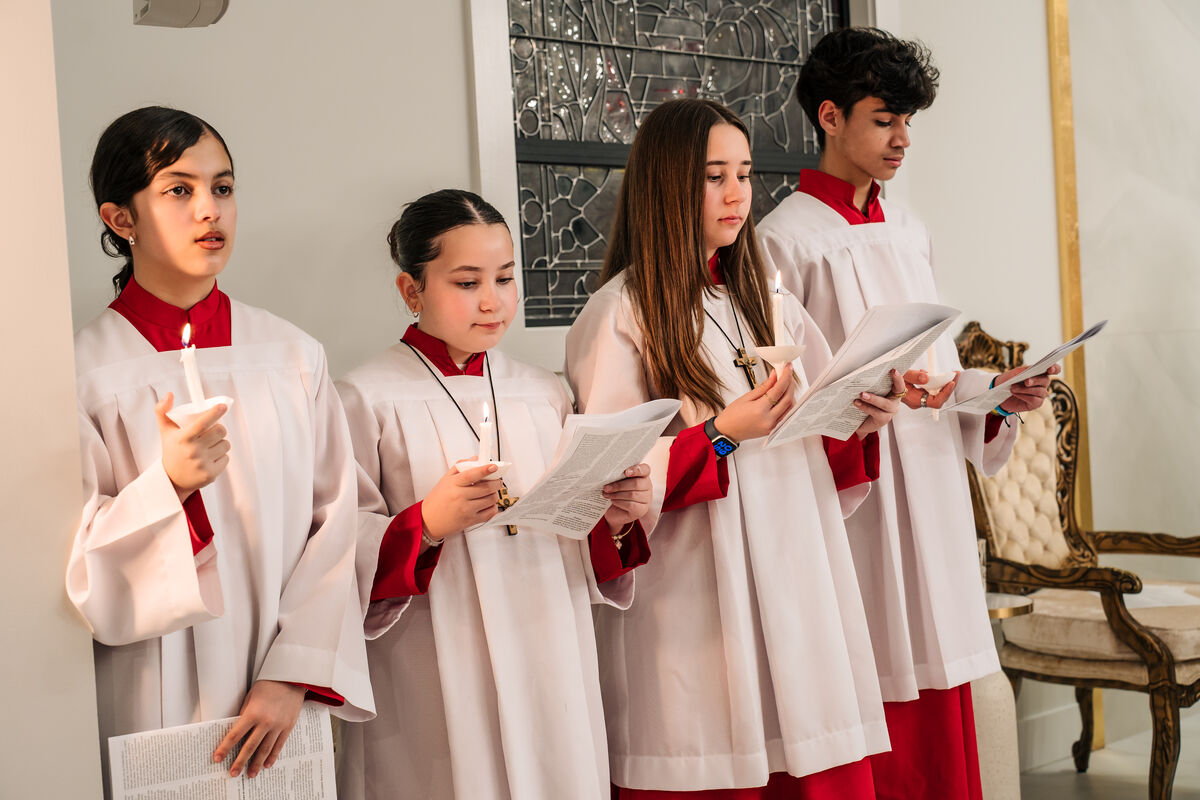 Young altar servers in white surplices and red cassocks sing by candlelight at the Easter Vigil